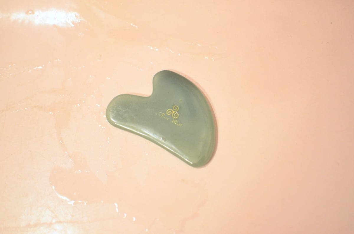 A jade gua sha stone resting on a dark textured surface